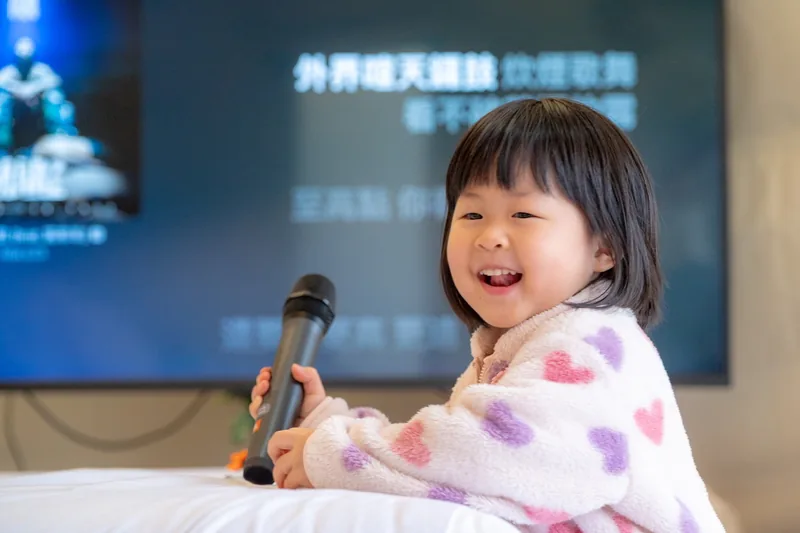 小朋友在熱氣球房拿著無線麥克風唱卡拉 OK，後方電視顯示歌詞