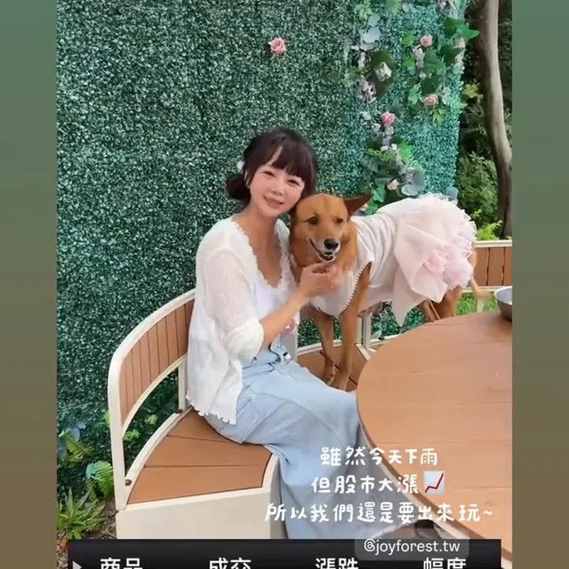 穿白色洋裝的女孩抱著棕色狗狗坐在綠色花牆前，旁邊有粉色裝飾