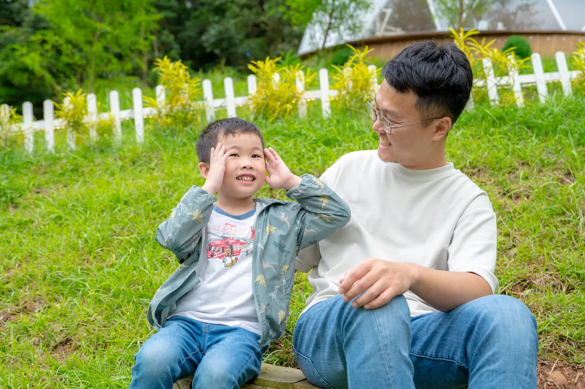 爸爸與兒子坐在草地上拍攝週末親子寫真