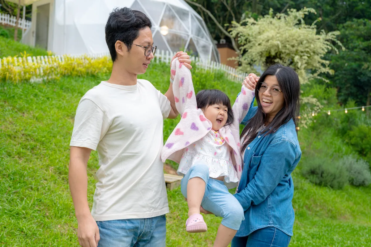 爸爸媽媽在草地上一起抱起女兒