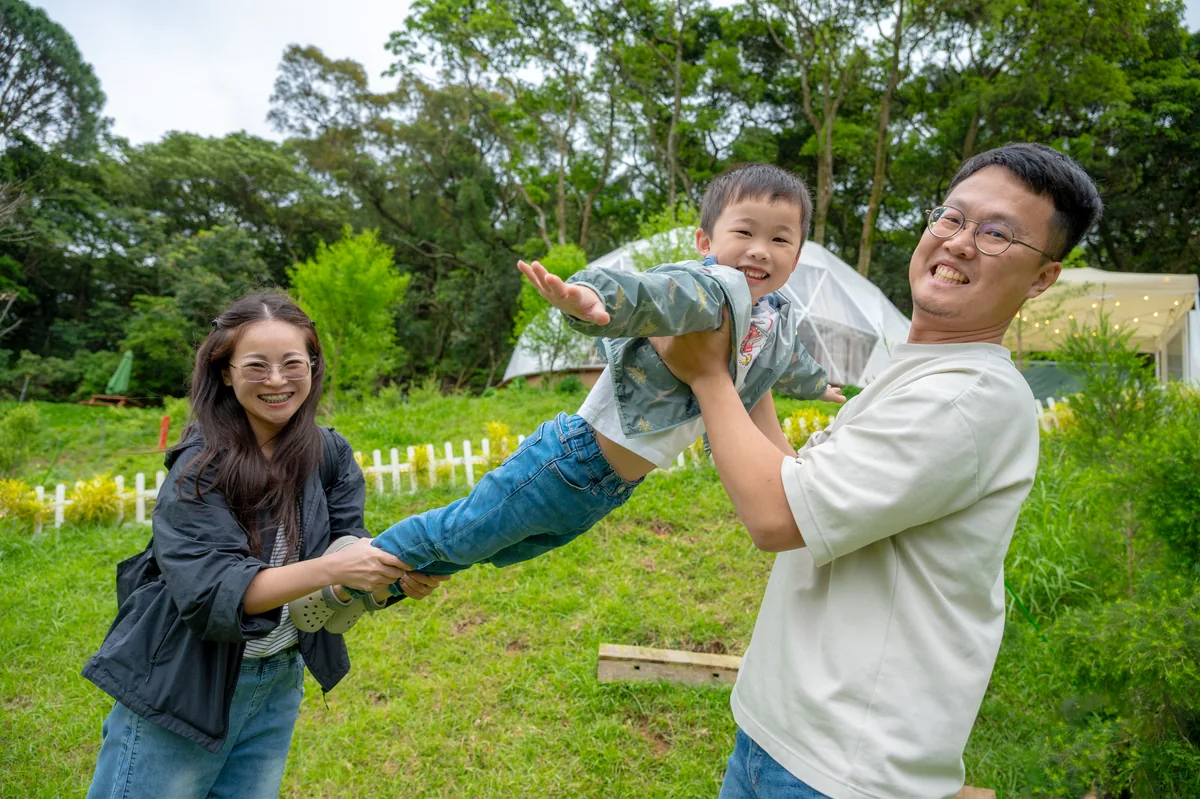 爸爸媽媽牽著兒子的手在草地上把他輕輕晃起